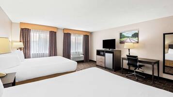 A hotel room with two beds, a desk with a chair, a television, and a window with curtains.