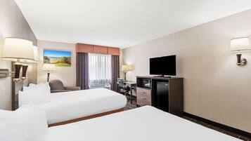 A hotel room with two beds, a desk, a television, and a window with curtains.