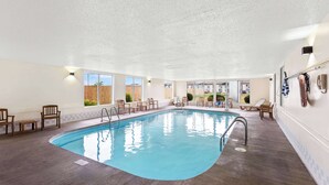 An indoor swimming pool with wooden chairs and a lifebuoy on the wall.