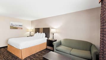 A hotel room with a bed, a green sofa, a nightstand with a lamp, and a small table.