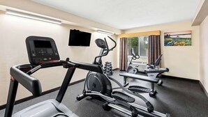 A gym with treadmills, an elliptical, and a stationary bike. There is a TV mounted on the wall and a window with curtains.