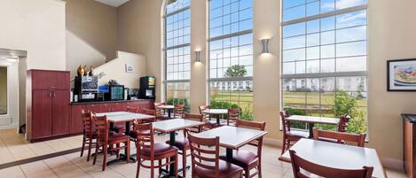 A spacious dining area with multiple tables and chairs, large arched windows, and a view of the outdoors.
