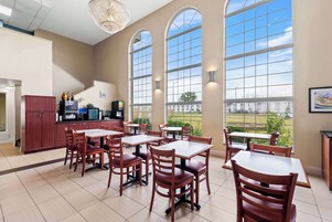 Un comedor amplio con varias mesas y sillas, ventanas arqueadas grandes y vistas al exterior.