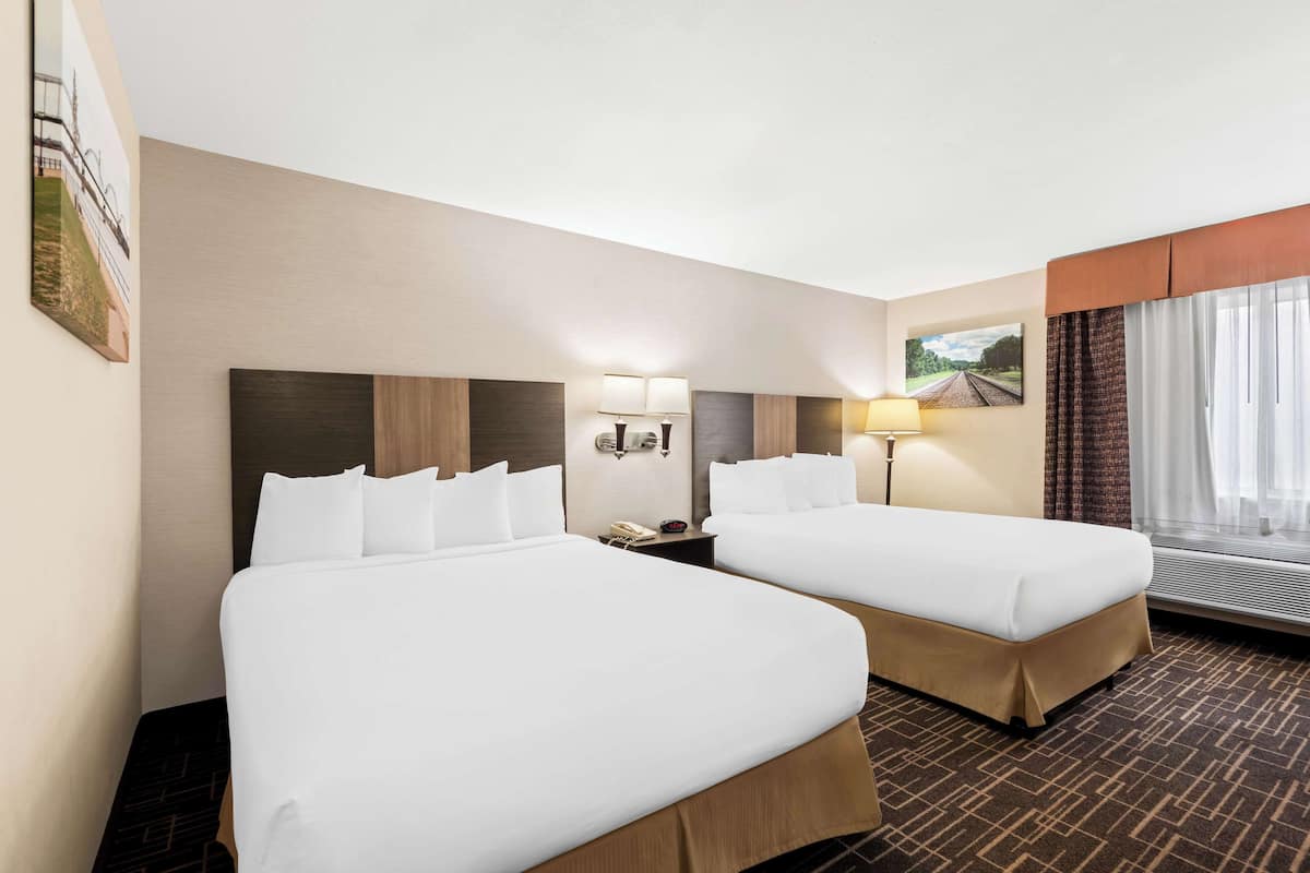 A hotel room with two beds, a nightstand, a lamp, and a window with curtains.