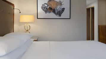 Una habitación de hotel con una cama bien tendida, una lámpara y una obra de arte abstracta enmarcada en la pared.