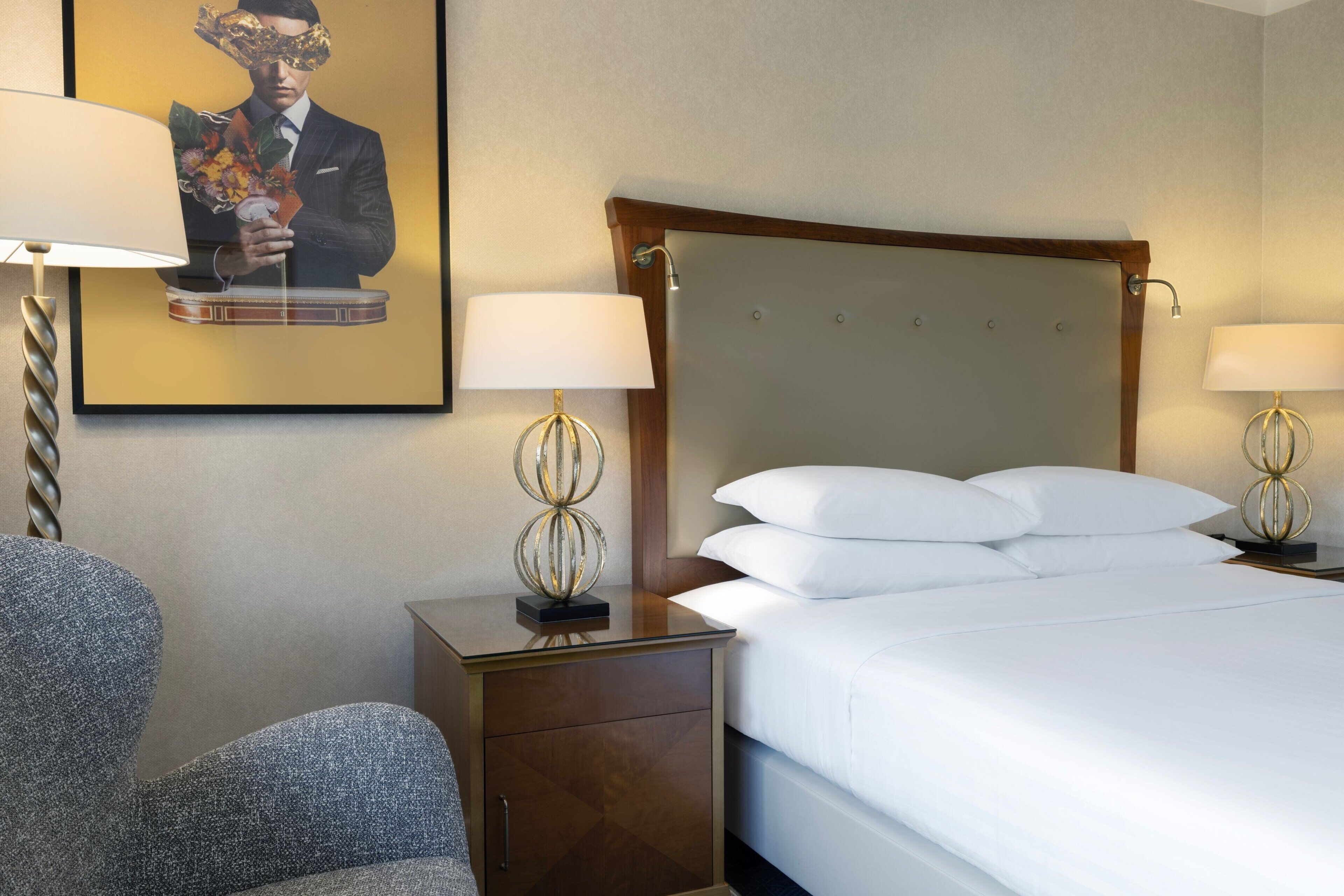 Ein Hotelzimmer mit einem großen Bett, zwei Nachttischen mit Lampen, einem Sessel und einem gerahmten Bild an der Wand.