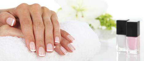 A hand resting on a white towel with a bottle of pink nail polish and a black bottle in the background.