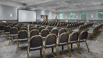 A conference room with rows of chairs, a projector screen, and windows with blinds.