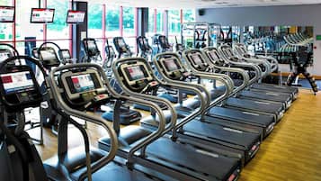 Un gimnasio con varias cintas de correr, bicicletas estáticas y máquinas de cardio.