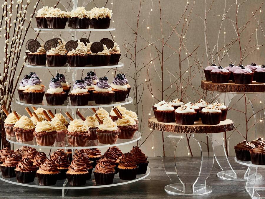 Ett vackert upplagt bord med olika sorters muffins och bakverk, arrangerade på genomskinliga stativ.