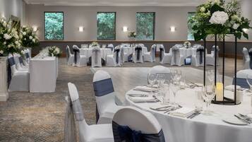 A banquet hall with round tables set for dining, white chairs with blue sashes, and floral centerpieces.