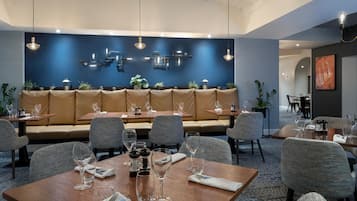 A restaurant with a blue wall, wooden tables, and cushioned seating.