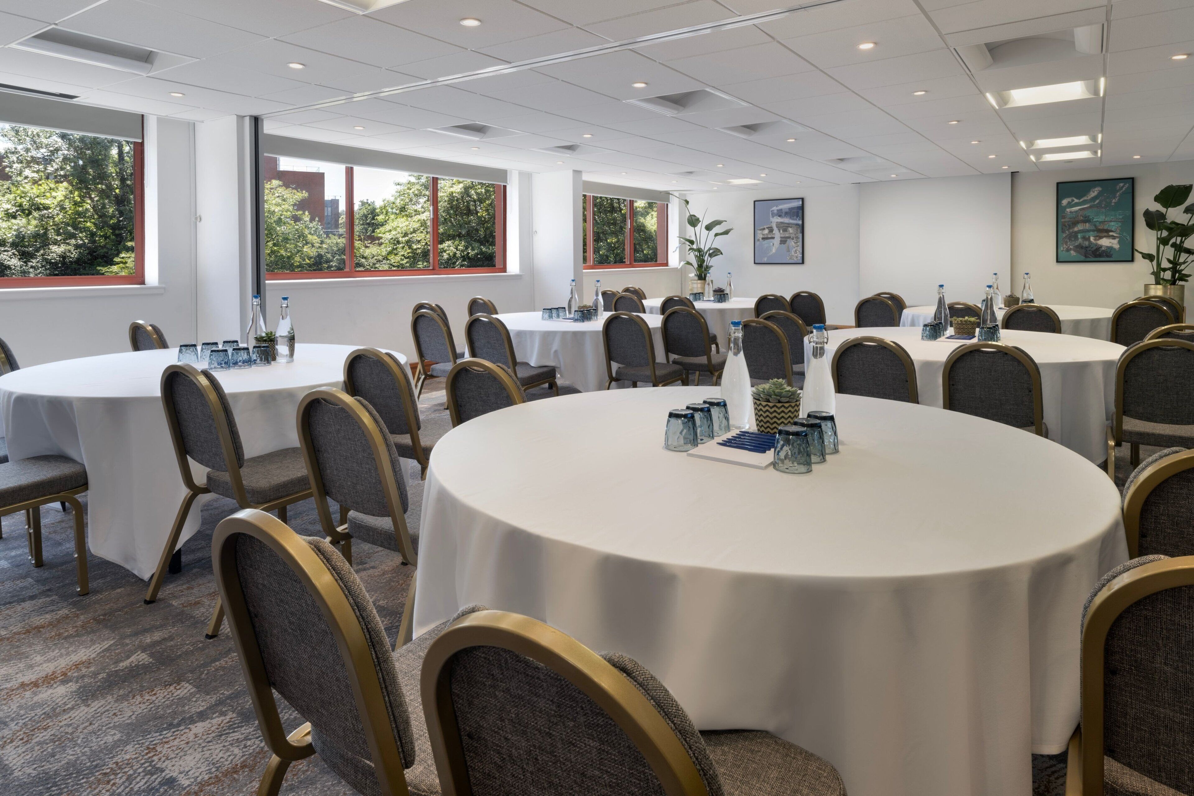 Une salle de conférence dotée de plusieurs tables rondes, chacune étant accompagnée de chaises et de couverts.