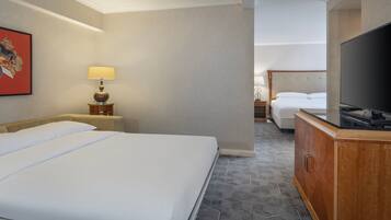 A hotel room with a large bed, a television, a bedside table with a lamp, and a small table with a decorative item.