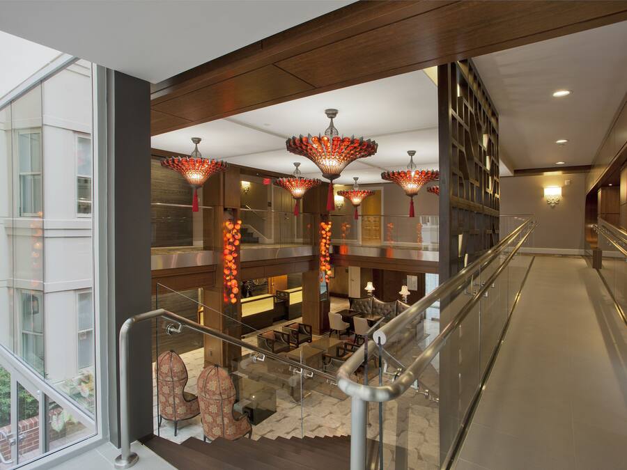 A modern hotel lobby with a glass railing, a staircase, and a seating area with a fireplace.