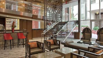 A hotel lobby with a bar area, seating, a staircase, and large windows.
