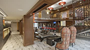 A spacious lobby with a modern design, featuring a seating area with sofas and chairs, a staircase, and a bar area.