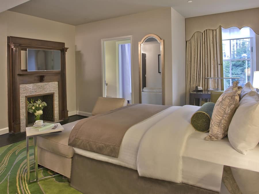 A bedroom with a large bed, a fireplace, a mirror, and a view of the outdoors.