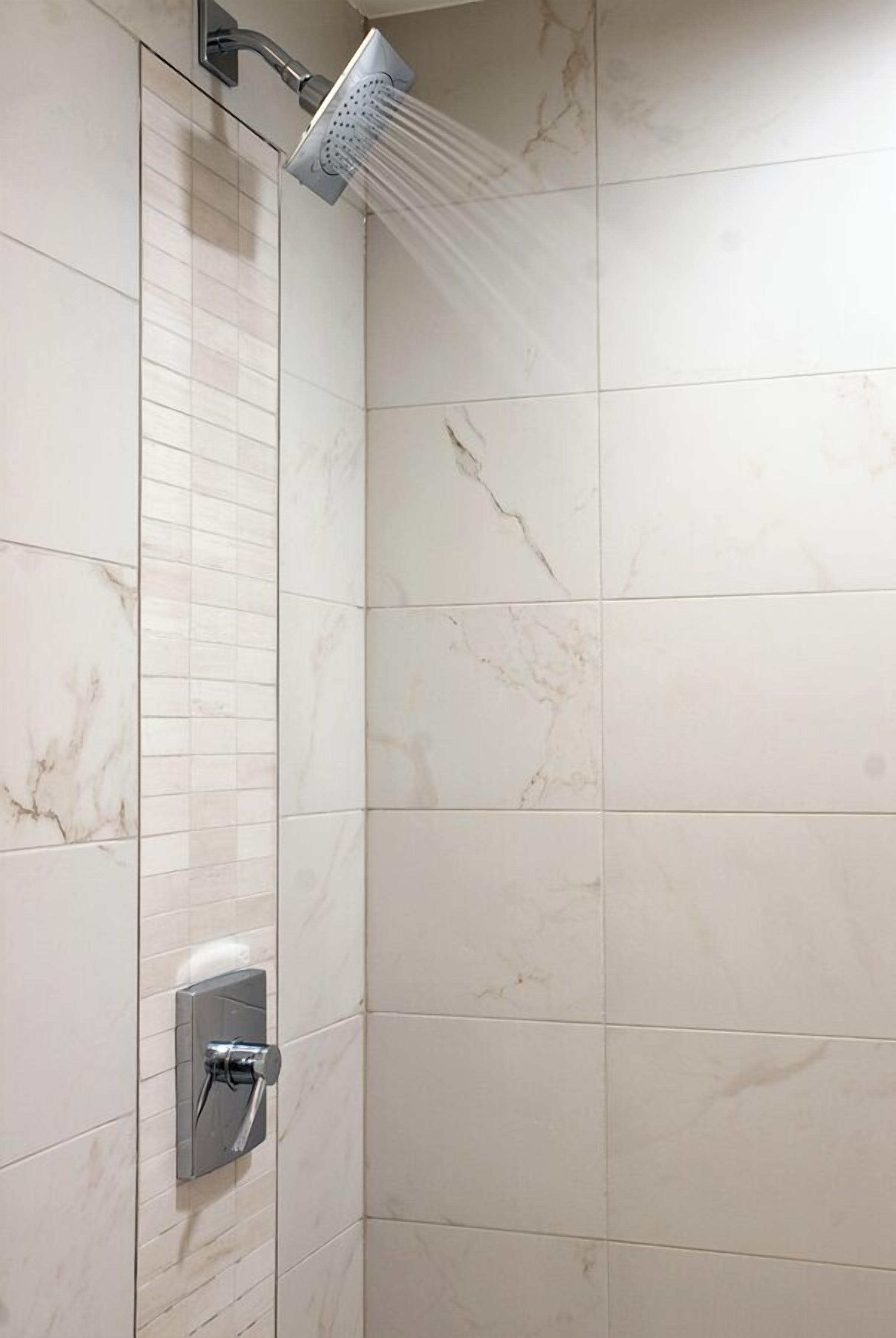 A shower with a handheld showerhead and a wall-mounted control panel.