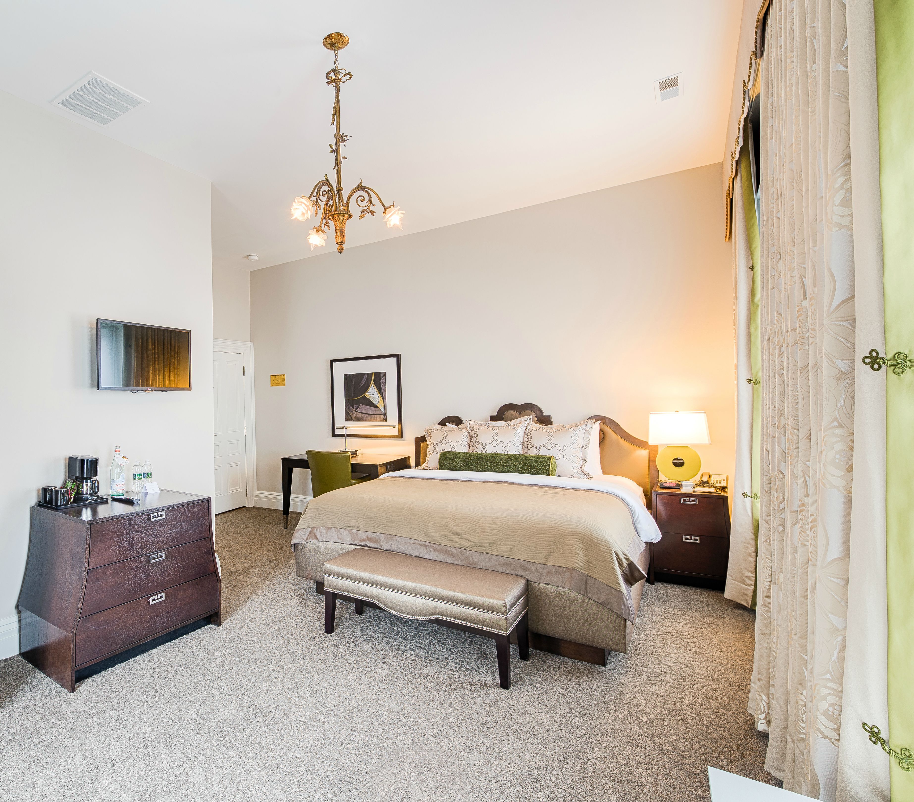 A bedroom with a bed, a bench, a dresser, a desk, a chair, a lamp, and a chandelier.