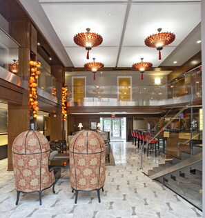 A spacious lobby with a grand staircase, ornate chandeliers, and classic armchairs.
