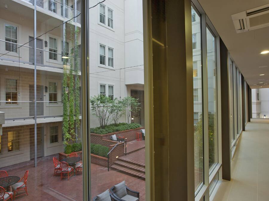 A corridor with large windows, a brick pathway, and outdoor seating with red chairs.