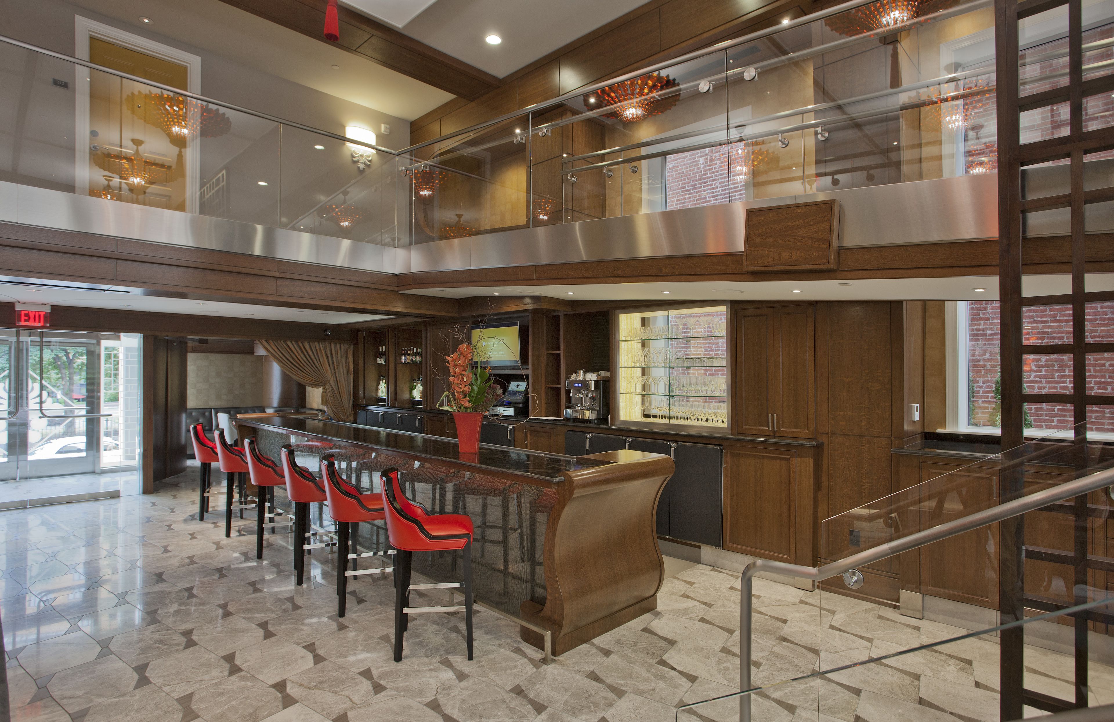 A modern hotel lobby with a glass railing, a bar area, and a seating section with red chairs.