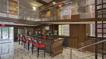 A modern hotel lobby with a glass railing, a bar area, and a seating section with red chairs.