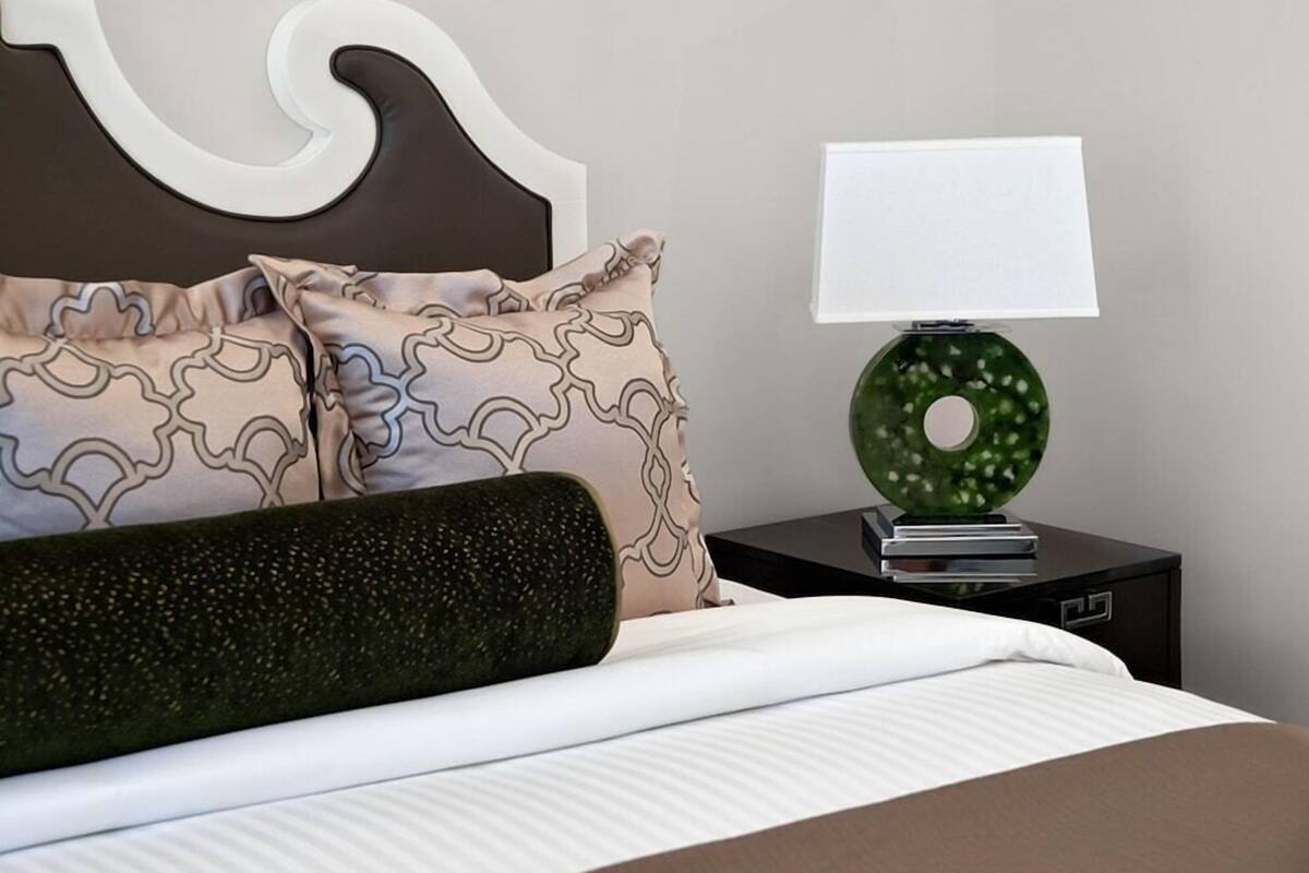 A neatly made bed with patterned pillows, a green decorative lamp, and a modern headboard.