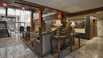 A modern hotel lobby with a reception desk, seating area, and a staircase leading to an outdoor terrace.