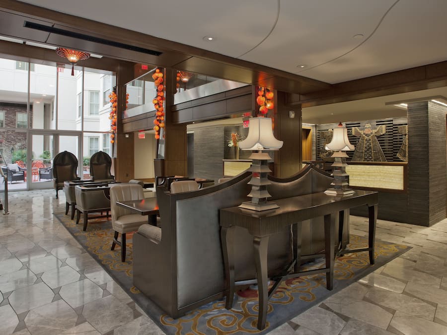 A modern hotel lobby with a reception desk, seating area, and a staircase leading to an outdoor terrace.