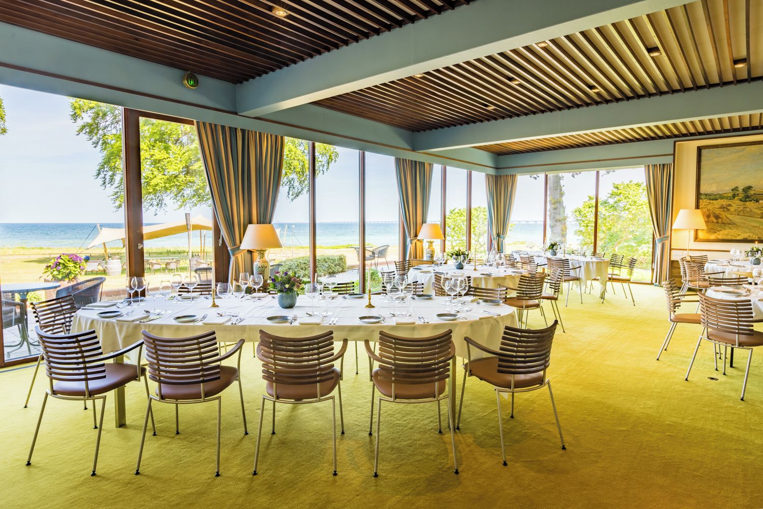 A restaurant with round tables, chairs, and a view of the sea.