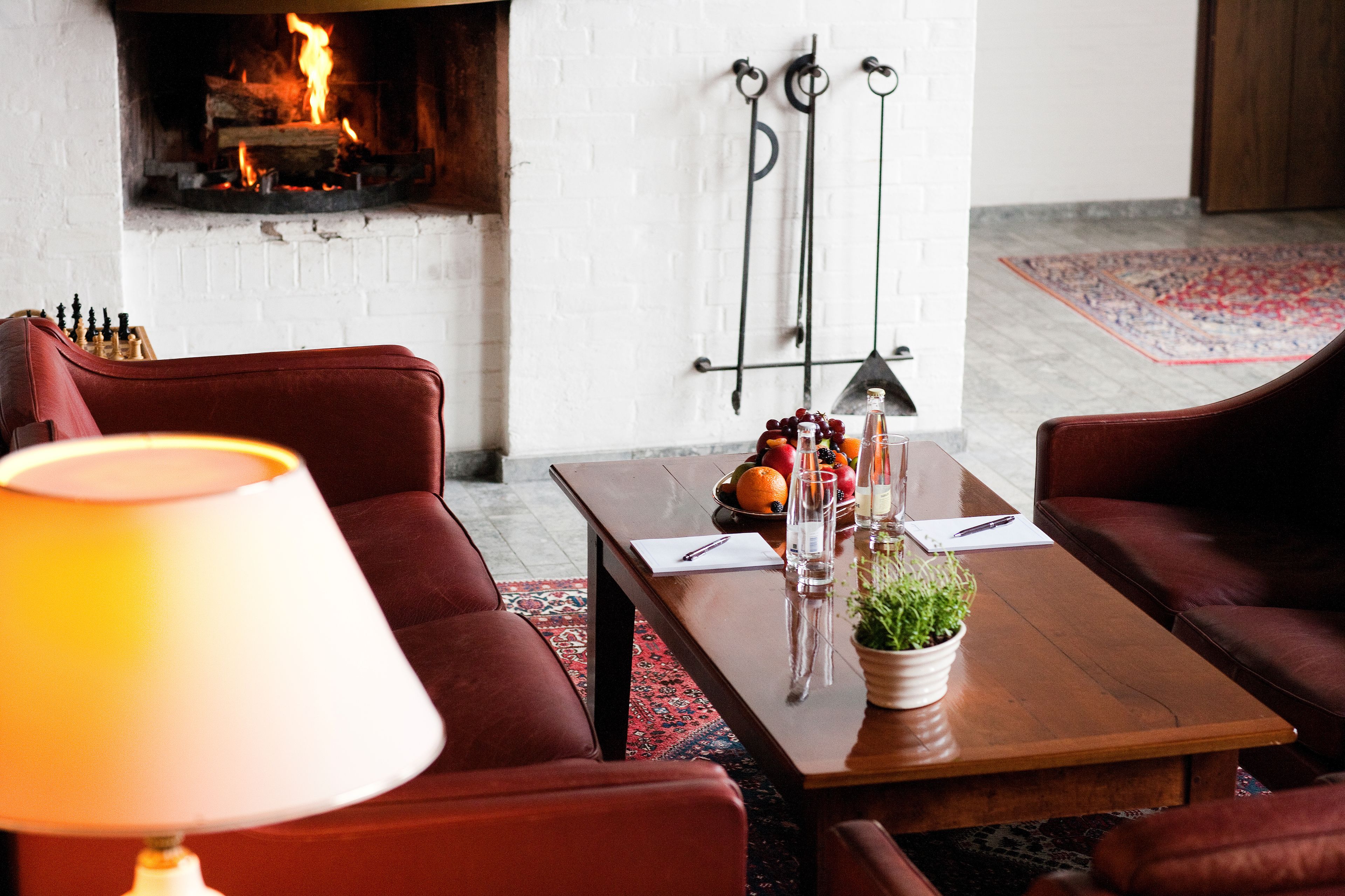A cozy living room with a fireplace, leather sofas, a coffee table with fruits and glasses, and a lamp.