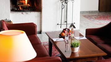 A cozy living room with a fireplace, leather sofas, a coffee table with fruits and glasses, and a lamp.