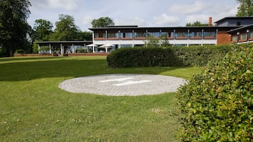 Un edificio moderno con tejado plano y grandes ventanales, rodeado de césped cuidado y una zona pavimentada circular.