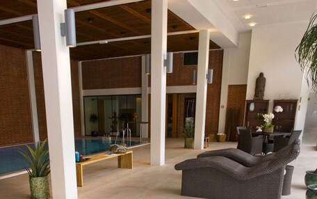 A hot tub in a spacious indoor area with a pool, lounge chairs, and a dining area.
