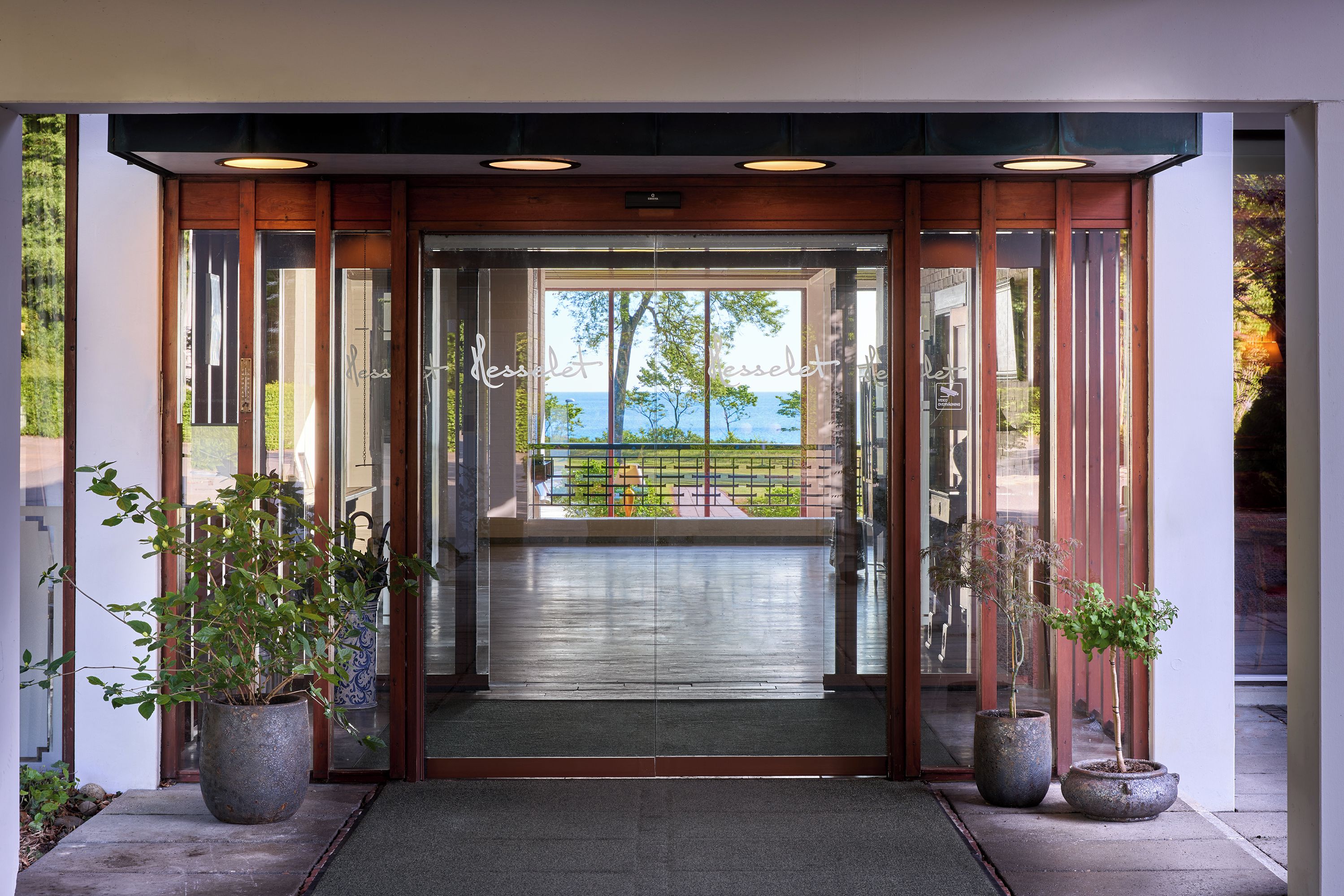 A hotel entrance with a glass door, a wooden frame, and a view of a green landscape.