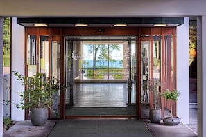 Entrada de un hotel con puerta de vidrio, marco de madera y vista a un paisaje verde.