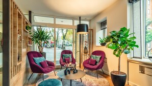 Una sala de estar moderna con una mesa de centro redonda, dos sillones rojos, un otoman azul y una planta grande en maceta.