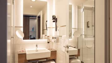 Un baño moderno con un espejo grande, dos lavamanos, una cabina de ducha de vidrio y un perchero para toallas.
