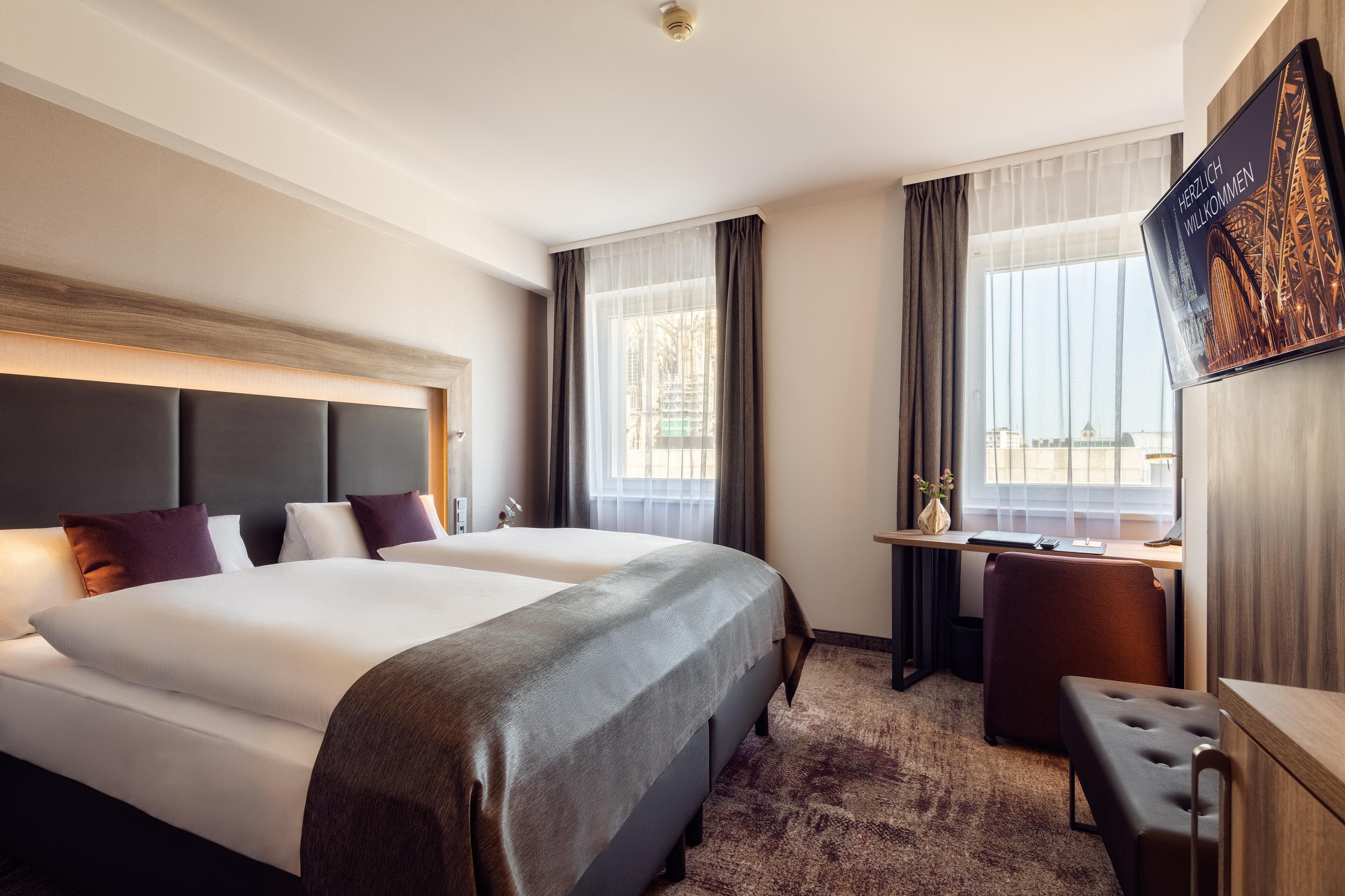 A hotel room with two beds, a desk, and a chair.