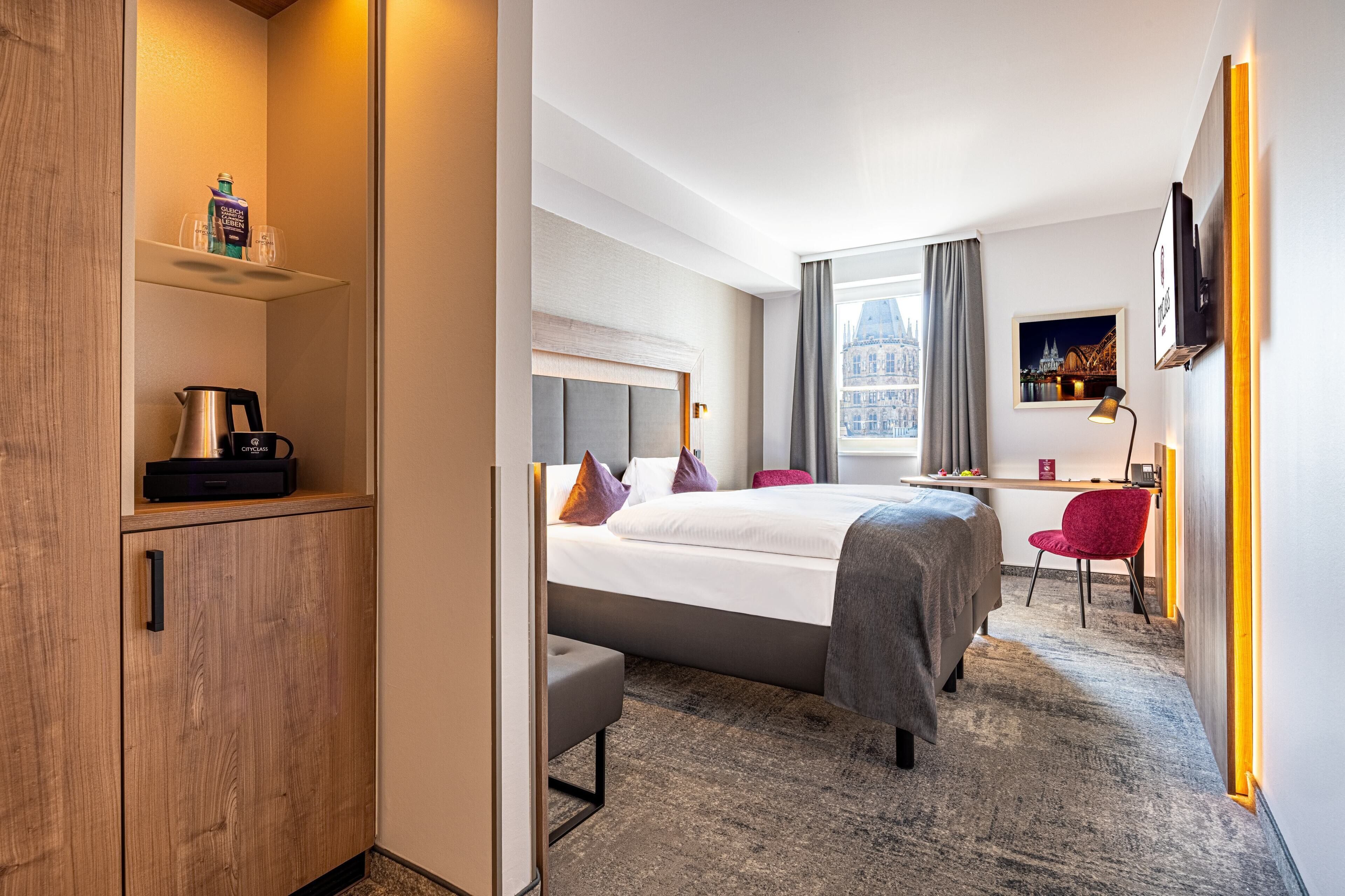 A hotel room with a bed, a desk, a chair, a TV, and a window with a city view.