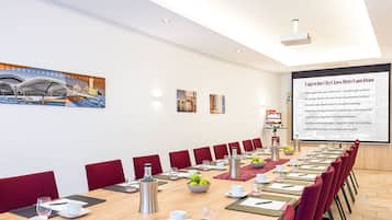 Una sala de conferencias con una larga mesa dispuesta para reuniones, equipada con tarjetas de identificación, vasos de agua y una pantalla de proyector mostrando texto.