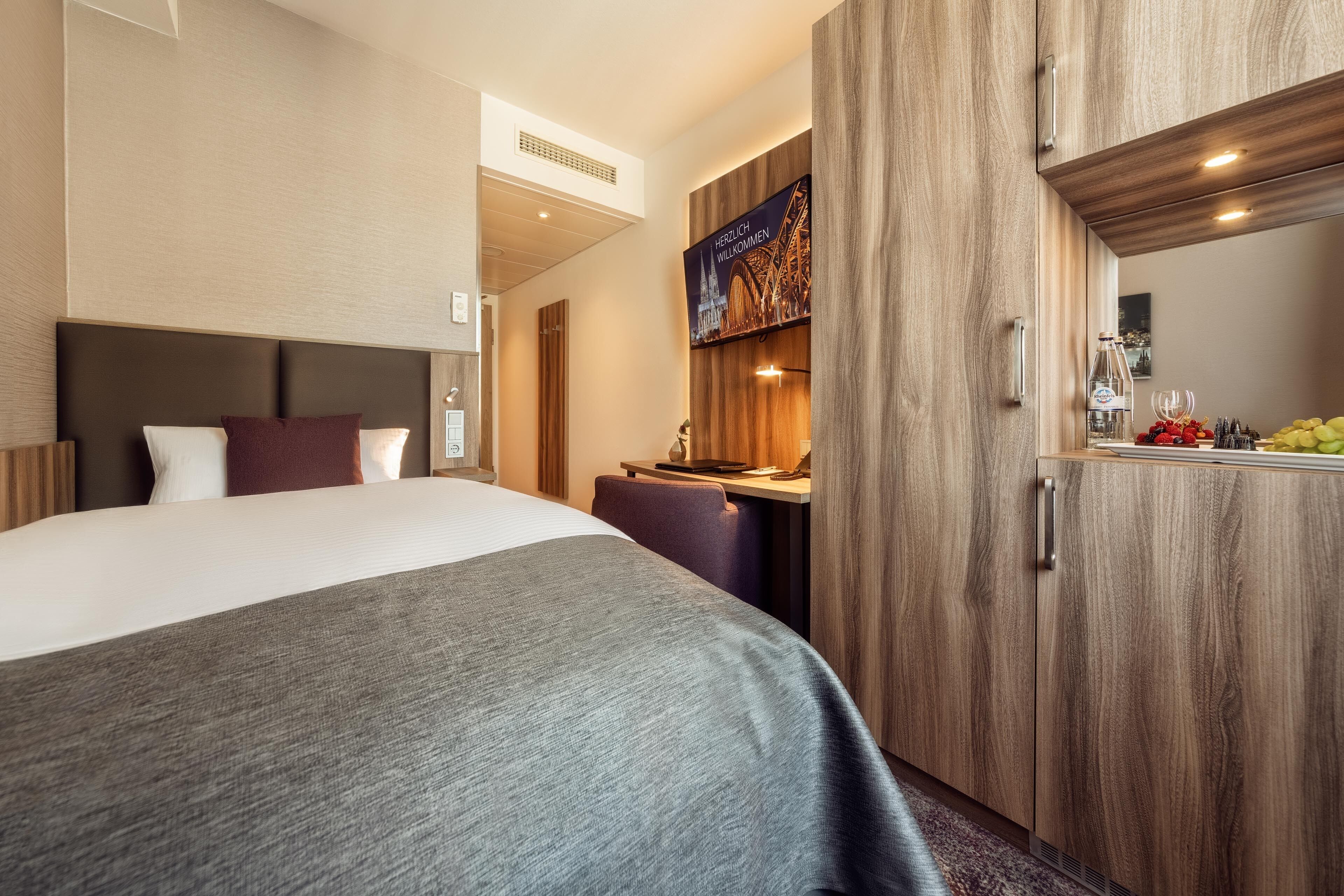 A hotel room with a large bed, a desk, and a wardrobe.