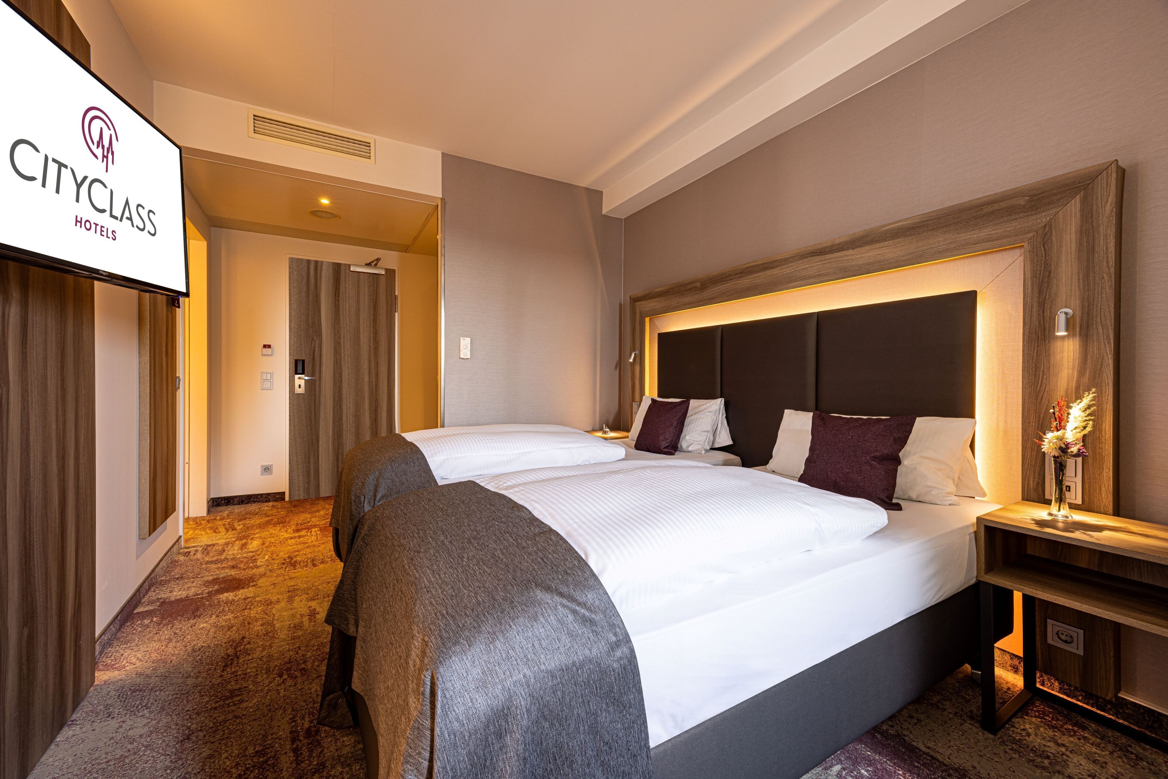 A CityClass hotel room with a large bed, a nightstand, and a wall-mounted TV.