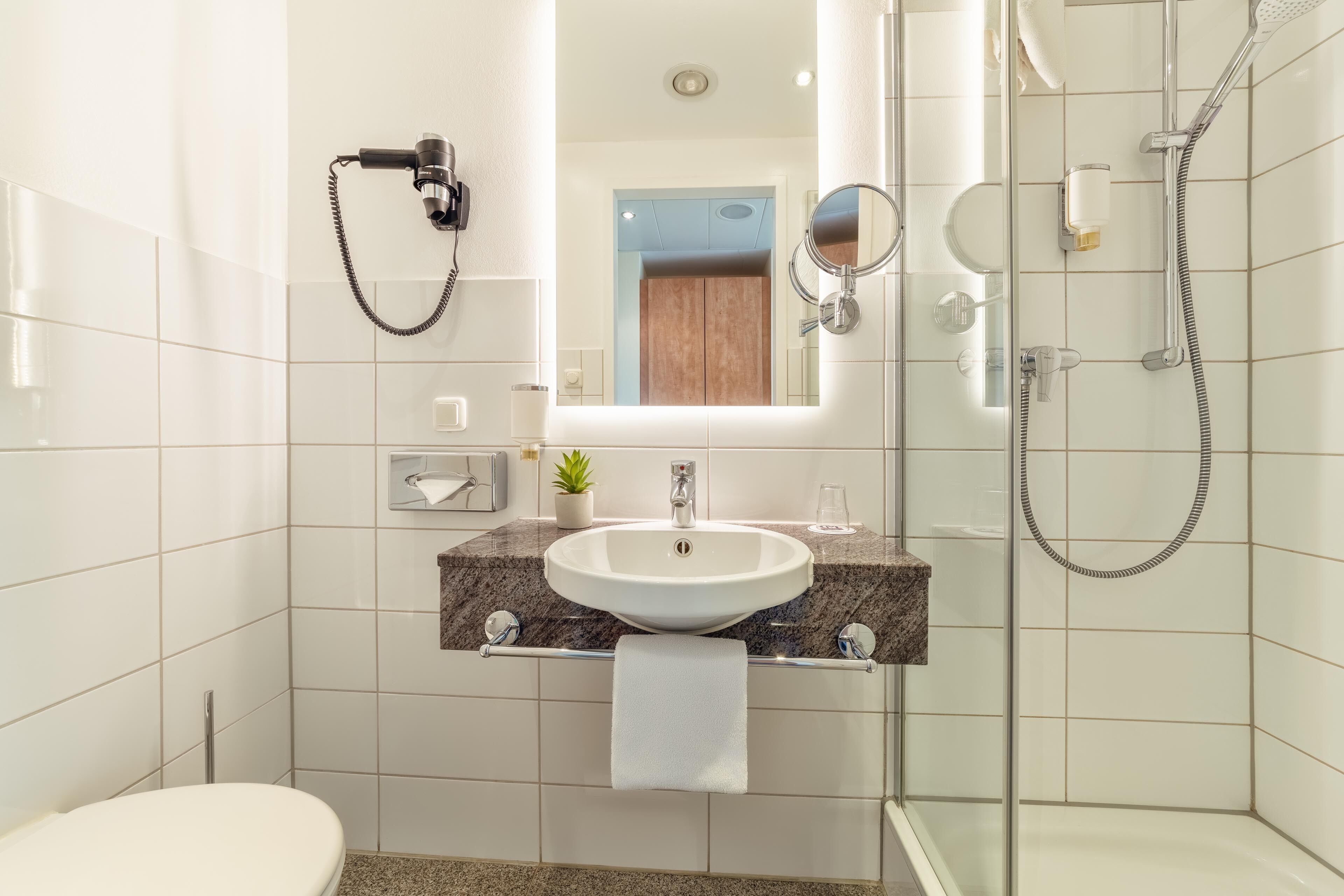 A modern bathroom with a sink, mirror, towel rack, and shower.