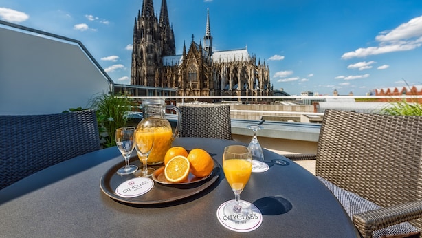 Mesa de comedor con una bandeja de jugo de naranja, vasos y naranjas, con vista a una catedral.