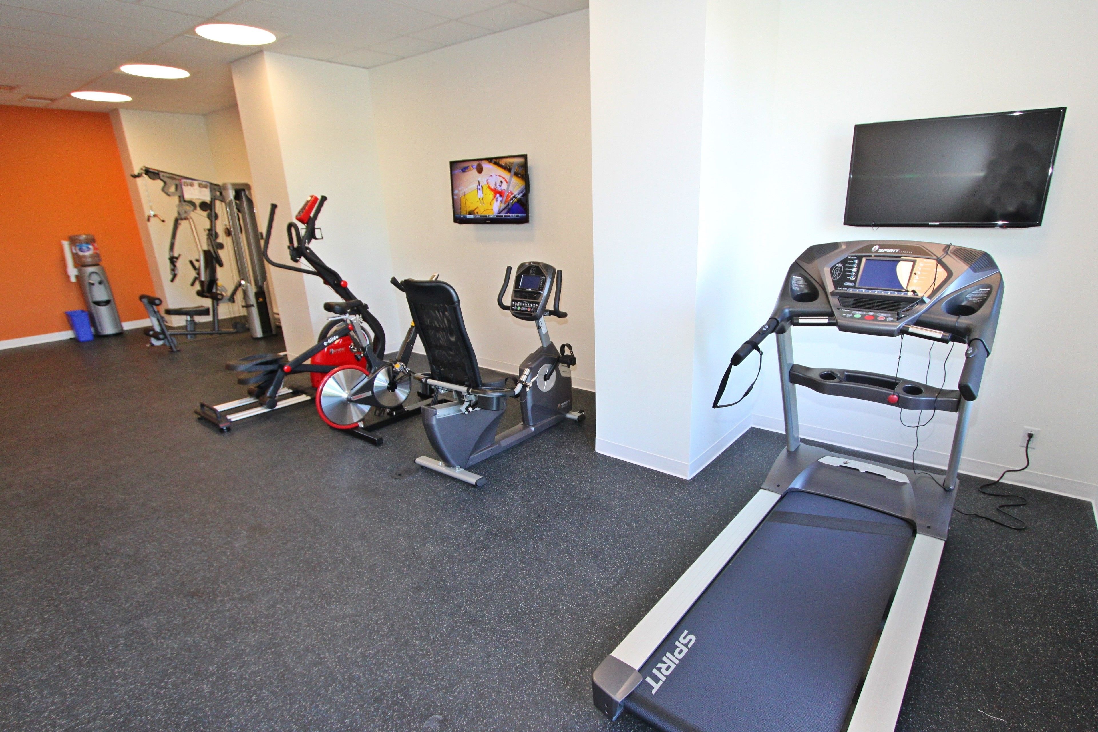 A gym with cardio equipment, a treadmill, and a TV on the wall.