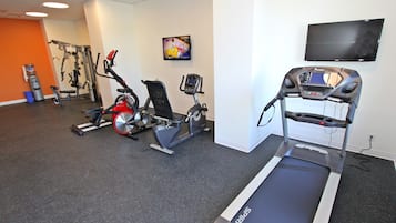 A gym with cardio equipment, a treadmill, and a TV on the wall.