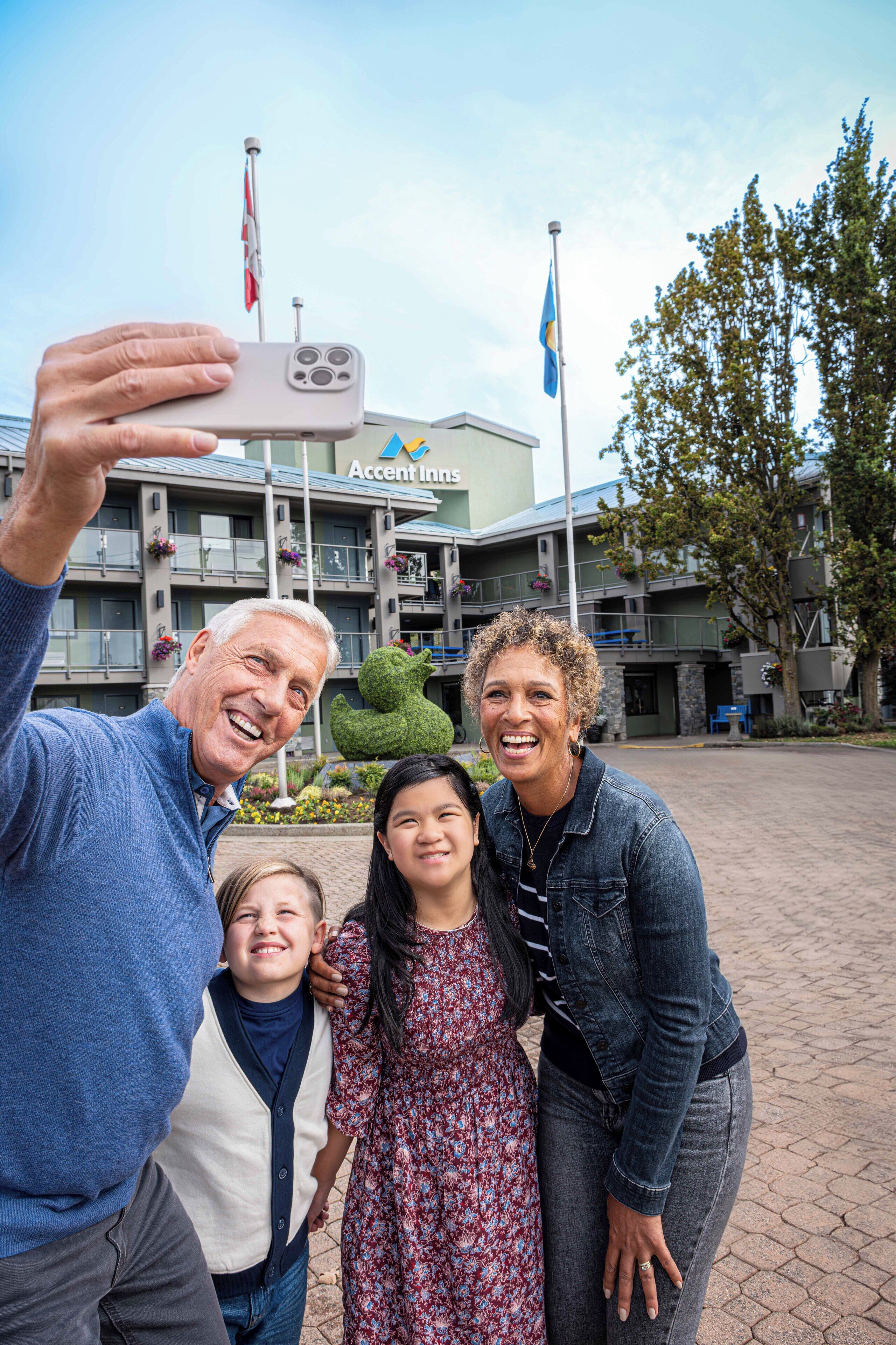 A family taking a selfie in front of a hotel with a sign that reads "Accent Inn."